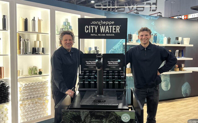 Promotional products trade fair Düsseldorf showcasing a water refill station with two smiling men.