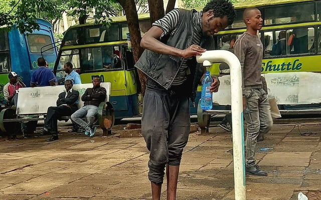 Person filling a bottle at a water tap near clean water Nairobi Kencom bus station.