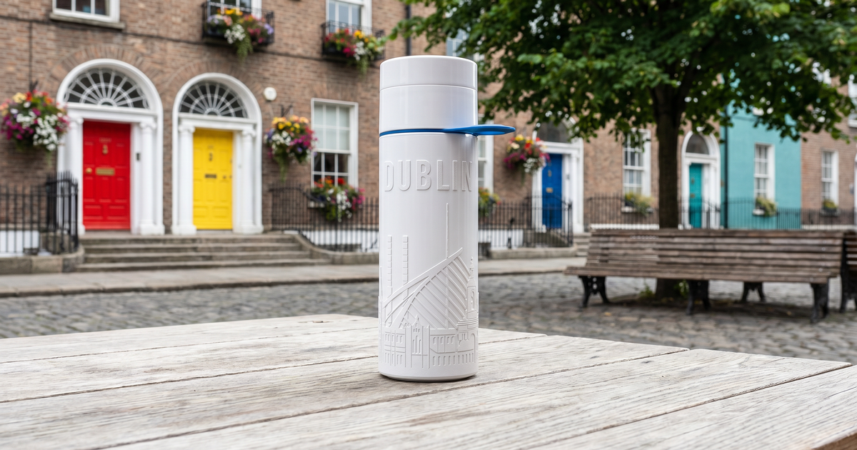 A reusable Dublin water bottle with skyline design on a wooden table in front of colorful doors.