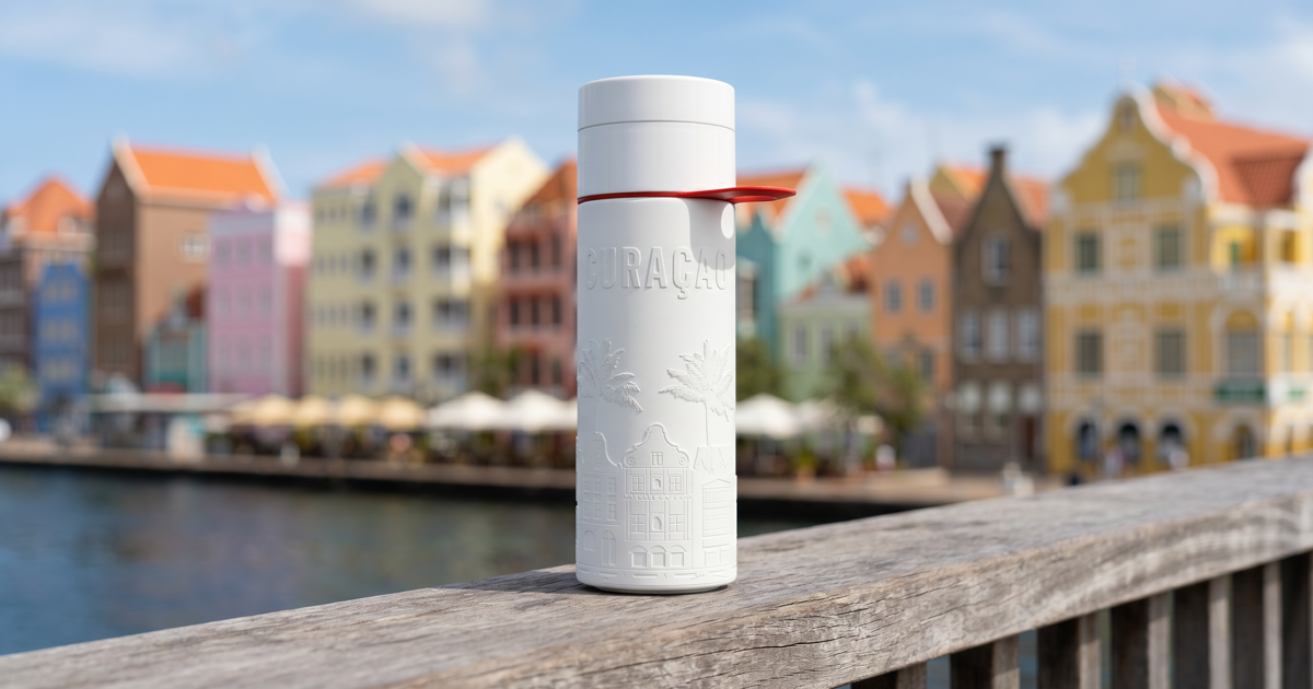 Herbruikbare Join the Pipe Curacao waterfles op een houten reling met de kleurrijke pastelhuizen van de Handelskade in Willemstad op de achtergrond.