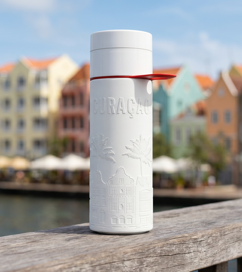 Herbruikbare Join the Pipe Curacao waterfles op een houten reling met de kleurrijke pastelhuizen van de Handelskade in Willemstad op de achtergrond.
